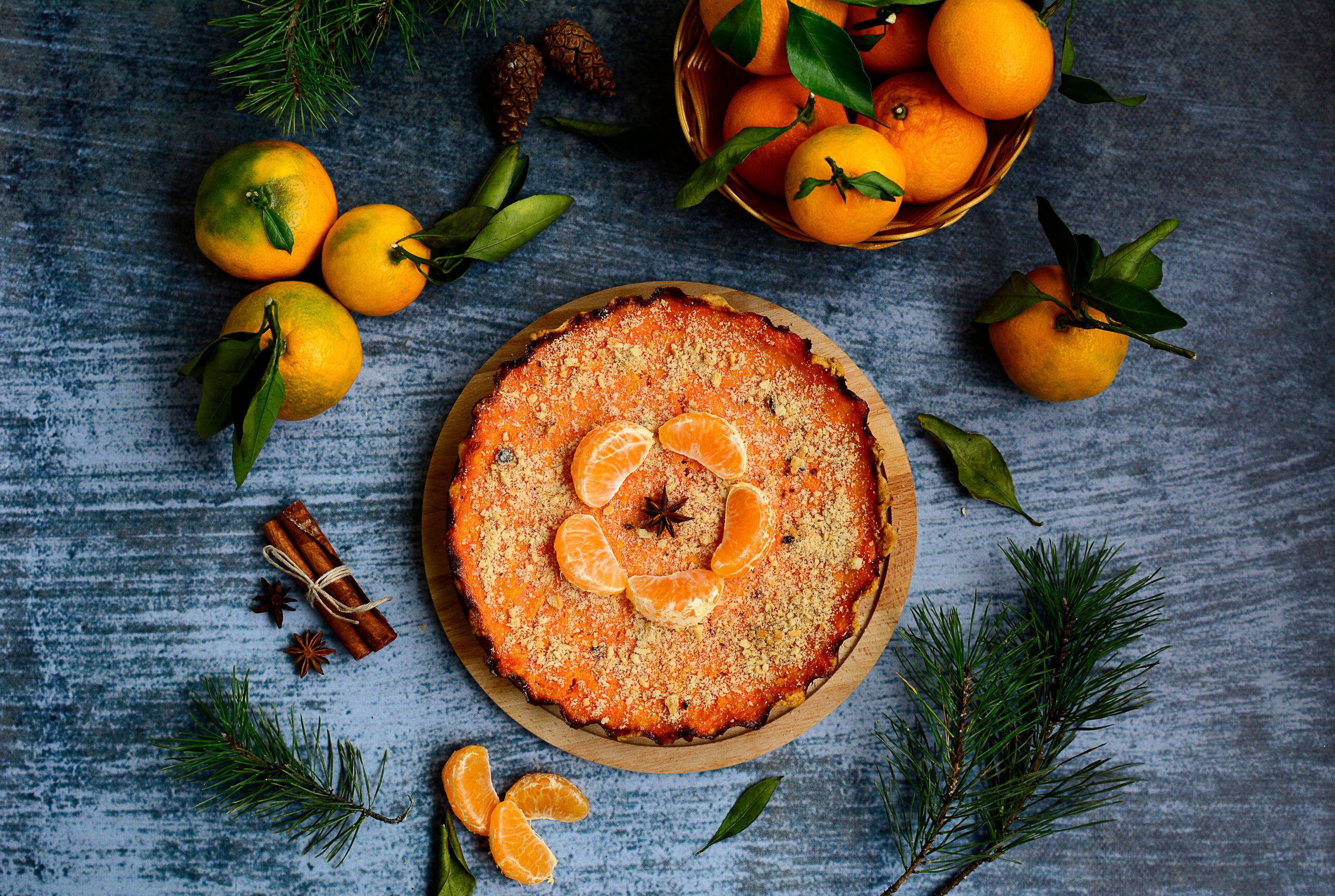 Pumpkin and citrus pie, tangerines, spruce twigs and cones, cinnamon sticks on a blue background, top view.