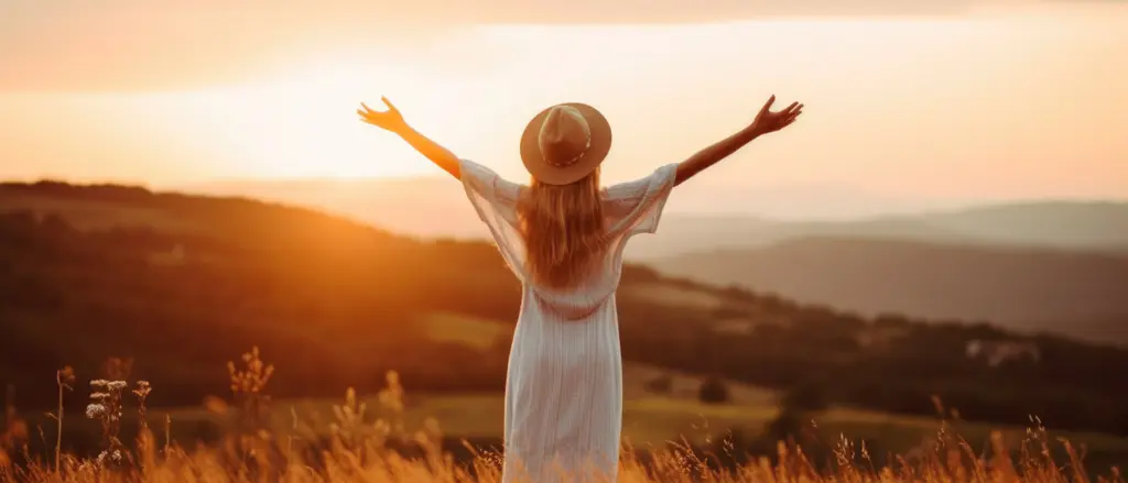 Eine Frau steht mit erhobenen Armen auf einem Berggipfel über den Wolken bei Sonnenuntergang – Erfolg, Freiheit und persönliche Potenzialentfaltung bei Zukunfts-Impuls.